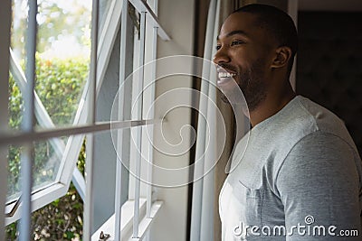 Thoughtful smiling man looking out through window at home Stock Photo
