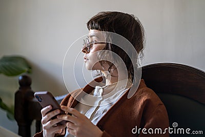 Thoughtful teen girl with smartphone looking concentrated while thinking over received message, info Stock Photo