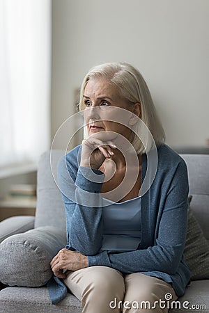 Thoughtful upset middle-aged woman sit on sofa at home Stock Photo