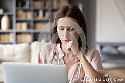 Thoughtful woman looking at laptop screen, pondering project Stock Photo