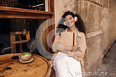 Thoughtful young african woman sitting on cafe terrace deaming with folders. Stock Photo