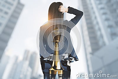 Thoughtful young businesswoman standing on blurry city background with mock up place and chess king. Success, strategy, think, Stock Photo