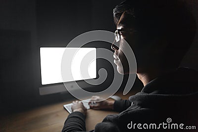 Thoughtful young man using blank screen computer in dark room Stock Photo