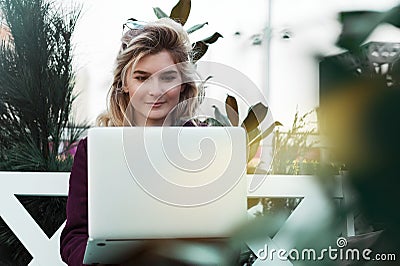 Thoughtful young woman in glasses using a computer, sitting on a bench in a city park. The concept of time is online and work in Stock Photo
