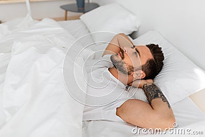 Thoughts in head not let fall asleep. Millennial man lying in bed and looking at ceiling, thinking of something Stock Photo