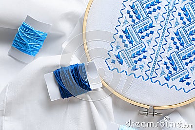 Threads and blue Ukrainian national embroidery on white fabric, top view Stock Photo