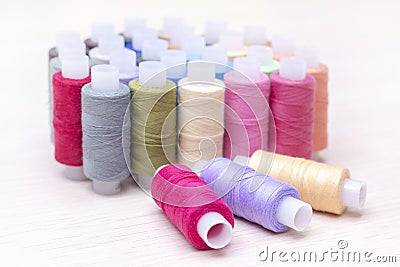 Threads on spools of different colors lie on a light wooden table. Three spools of thread are lying. Stock Photo