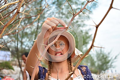 Girl got stuck on prickly thorn. Sharp needles on tree. Dense spiny shrub with thorns. The child cut his finger autdoor. Rose. Stock Photo