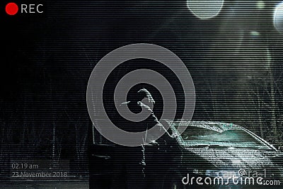 A threatening hooded man looking into a car at night. Photoshop edit to look like CCTV image Stock Photo
