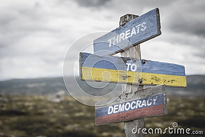 threaths to democracy text quote on wooden signpost outdoors on nato colored flag, ukrainian flag and russian flags Stock Photo