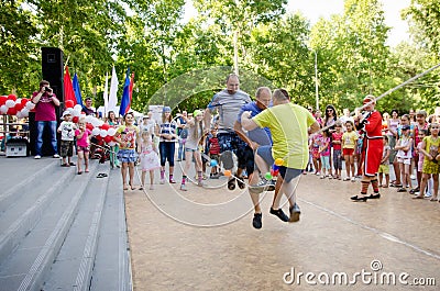 Three adult men at the same time jumping over rope which girls in pirate costumes hold at pirate party Editorial Stock Photo