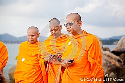 Three adult monk tourist wearing glasses and a orange dress with a camera and a phone in Thailand on Koh Samui Editorial Stock Photo