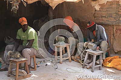Three African young men working at a souvenir factory in the poorest district of Nairobi - Kibera are sitting on chairs and workin Editorial Stock Photo
