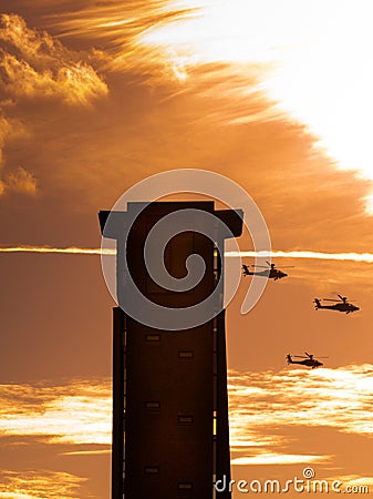 Three apache helicopters flying past a tower with clouds Stock Photo