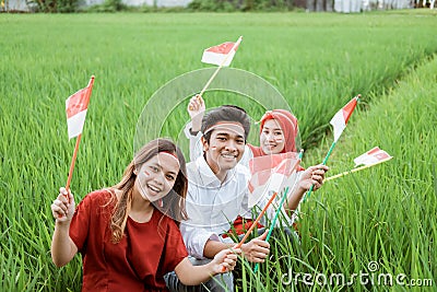 Three Asian friendly smile posing hold a small flag sitting in the middle of rice fields Stock Photo