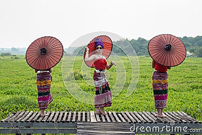 Three Asian Thai Lanna woman in traditional dress hand hold paper umbrella act like model on wooden bamboo bridge with overcast Stock Photo