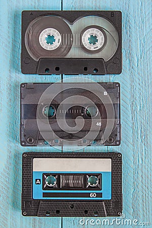 Three audio cassettes in black cases lie on a blue wooden background Stock Photo