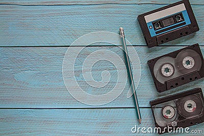 Three audio cassettes and a simple pencil lie on a blue wooden background. Space for the text Stock Photo