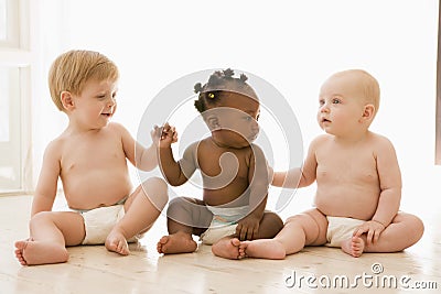 Three babies sitting indoors holding hands Stock Photo