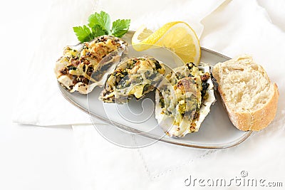 Three baked oysters Rockefeller with spinach and cheese on a small plate with lemon, bread and parsley garnish, festive appetizer Stock Photo