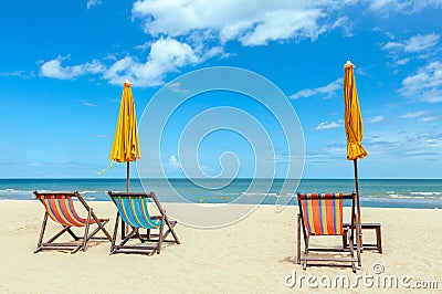 Three beach chairs with sun umbrella on beautiful beach with cloudy blue sky. Stock Photo