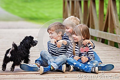 Three beautiful adorable kids, siblings, playing with cute little dog in the park Stock Photo