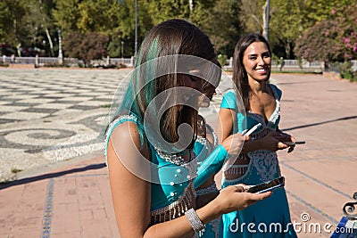 Three beautiful adult belly dancers are checking their mobile phones. They are looking at messages, e-mails and photos. Mobile Stock Photo