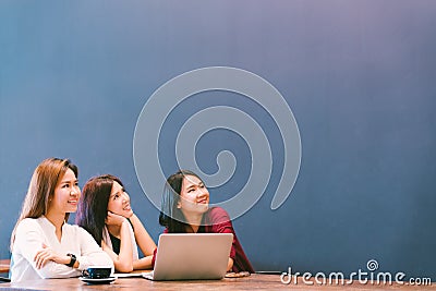 Three beautiful Asian girls looking upward to copy space while working at cafe, modern lifestyle with gadget technology concept Stock Photo