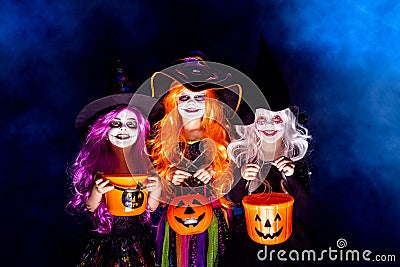 Three Beautiful girl in a witch costume on a dark background in smoke scaring and making faces Stock Photo