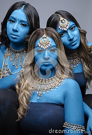 Three South Asian women painted blue and wearing gold jewellery Stock Photo