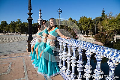 Three belly dancers dressed in light blue leaning on the railing of a bridge. They are talking to each other and looking at the Stock Photo