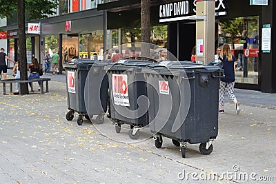 Three big black garbage bins on wheels belonging to a shop standing in the city center of Mannheim Editorial Stock Photo