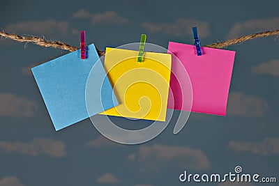 Three blank colorful notes clipped on twine clothesline with clothespins in front of beautiful blue sky. Stock Photo