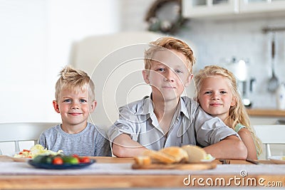 Three blonde kids twoboys and girl on kitchen at home. Family eating healthy food , green salad on plates. Looking at Stock Photo