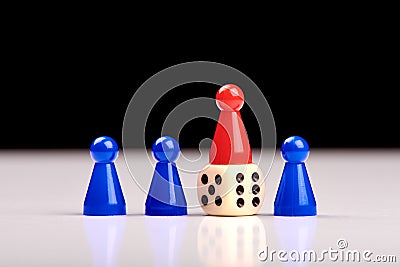 Three blue game pieces and between them one red piece stands on a dice as a winner or leader. Black and white background Stock Photo