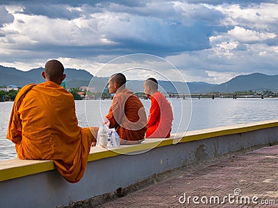 Three Buddhist monks sit next to the Preaek Tuek Chhu River at Kampot, Cambodia Editorial Stock Photo