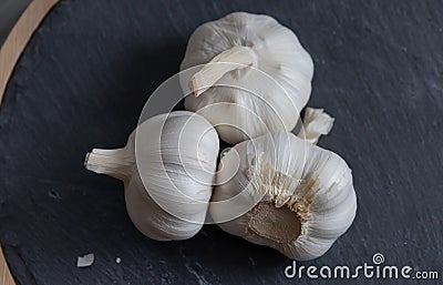 Three bulbs of garlic lie on a stone cutting board. Close-up. View from above Stock Photo
