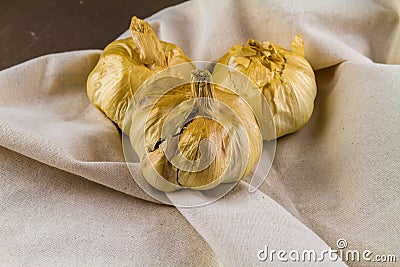 Three smoked garlic bulbs on hessian cloth surface Stock Photo