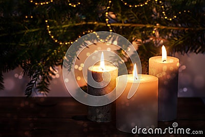 Three burning candles in front of dark fir branches with Christmas decoration and bokeh bubbles, seasonal holiday greeting card, Stock Photo