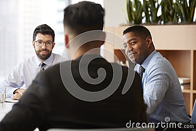 Three Businessmen Sitting Around Table Meeting In Modern Open Plan Office Stock Photo