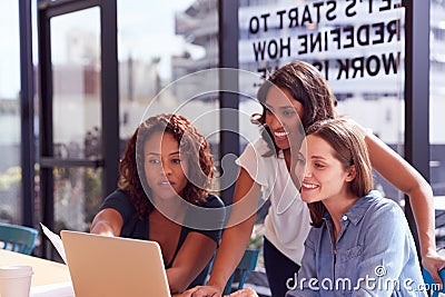 Three Businesswomen With Laptop At Desk By Window In Office Collaborating On Project Together Stock Photo
