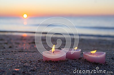 Three candles in shape of heart burn on sand on the sea beach near the sea waves Stock Photo