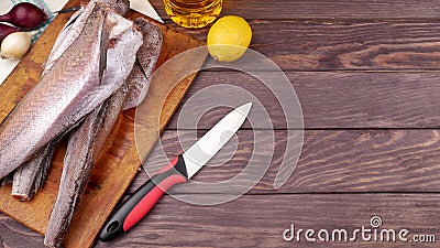 Three carcasses of fresh-frozen hake, pollock fish, on a cutting board on a wooden table. Stock Photo