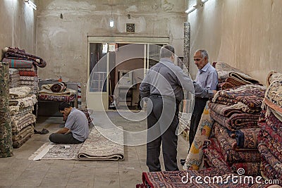 Three carpet sellers discussing and praying in a rug shop in the Yazd Khan bazaar. Carpets are of the main iconic exports of Iran Editorial Stock Photo