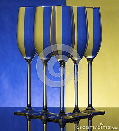 Three champagne glasses on a shiny surface with water that distort yellow and blue background Stock Photo