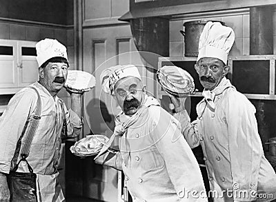 Three chefs holding pies for a fight in the kitchen Stock Photo