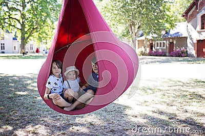 Three children, boys swinging in a big cloth swing in a park Stock Photo