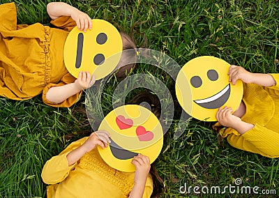 Three children lying on the grass are holding cardboard emoticons Stock Photo