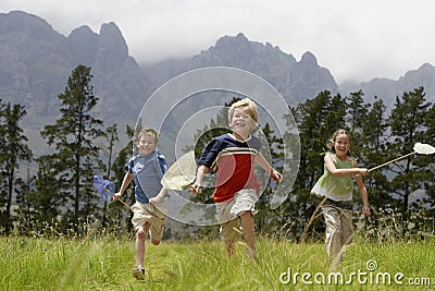 Three children 7-9 running through field with butterfly nets. Stock Photo