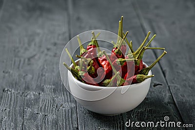 Three chilli pods and a bowl of peppers on a dark wooden table. The view from the top Stock Photo